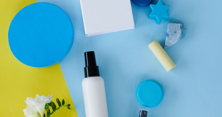 Flat lay view of skincare and cosmetic products, including white spray bottles, cream jars, and blue geometric display props arranged on a split yellow and light blue background, showcasing top beauty offers on sinibuy.com.
